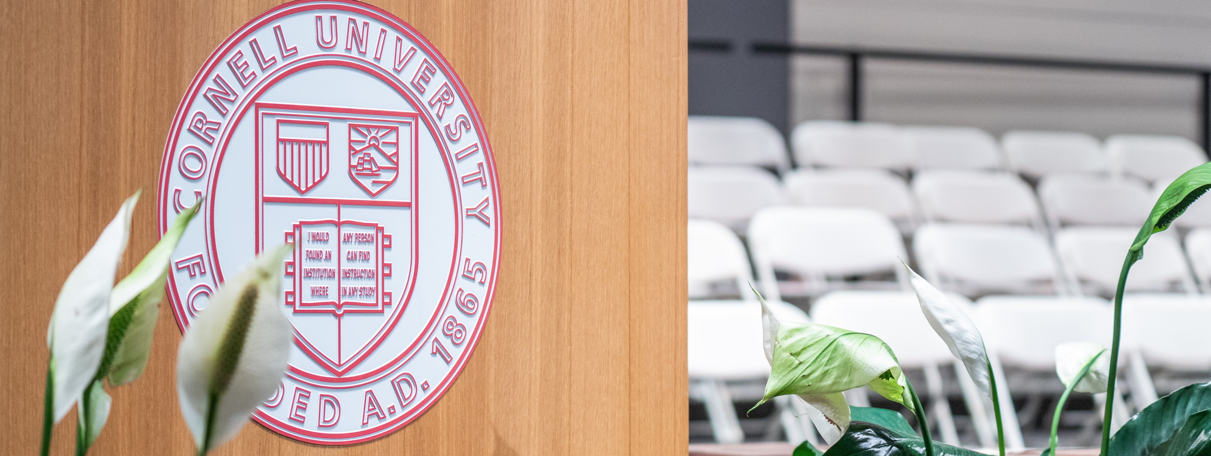 Podium with Cornell logo and empty white chairs blurred in the background