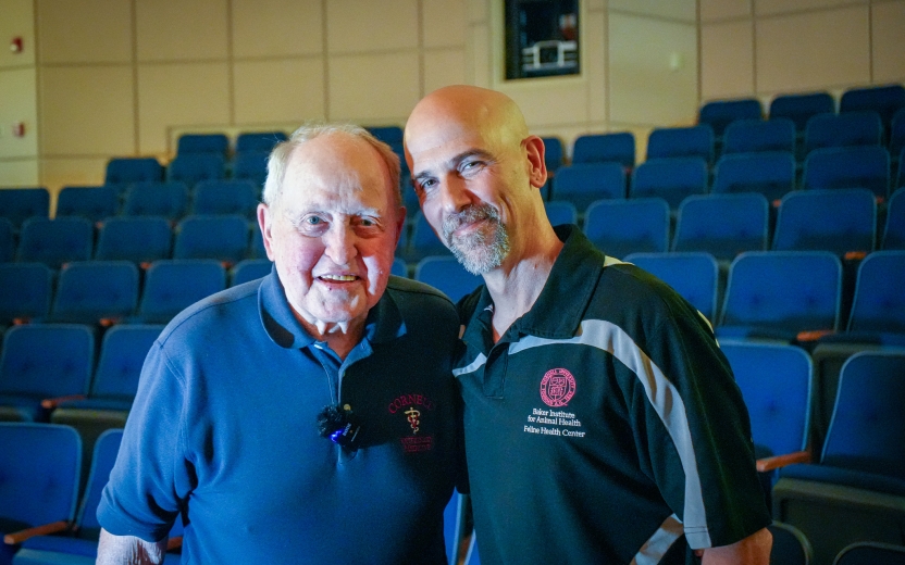 Two men stand in the Thaw Lecture Hall at the Baker Institute. 