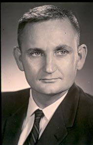 A black and white photo featuring the headshot of a young man in a dark suite.