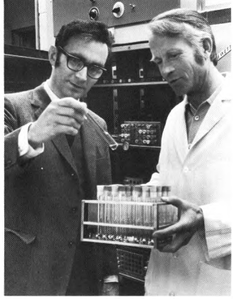 A black and white photo shows two men working in a lab at the Baker Institute. 