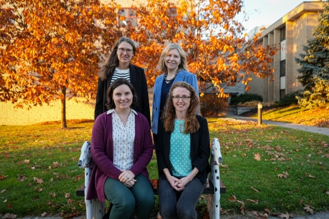 A group shot of four women standing outside the Baker Institute in the fall. 