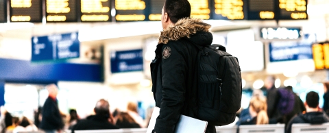 A man walking in an airport with a black bag on his back and a laptop in one hand.