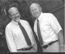 Two men standing next to each other in white shirts and dark ties. 