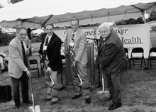 A black and white photos featuring four men in suites holding shovels. 