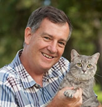 A photo of a man wearing a striped shirt holding a cat outside. 