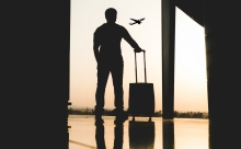 silhouette of a man holding a suitcase looking at a plane taking off