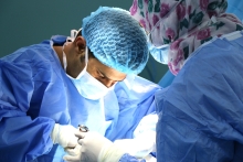 Two surgeons in blue gowns and caps performing a medical procedure under bright operating lights