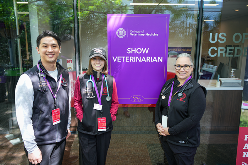 Student and two veterinarians standing next to clinical booth