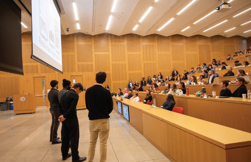 student presenters standing in front of audience in lecture hall 