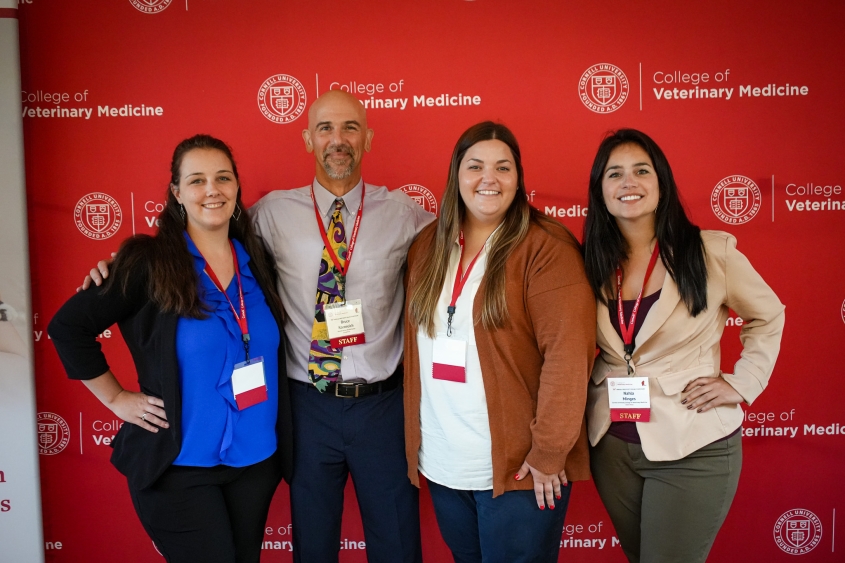 Four people, including one man and three women stand in front of a Cornell back drop.