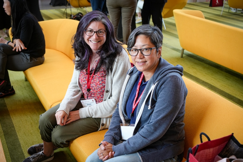 Two women sit and chat on yellow couches inside the CVM atrium.