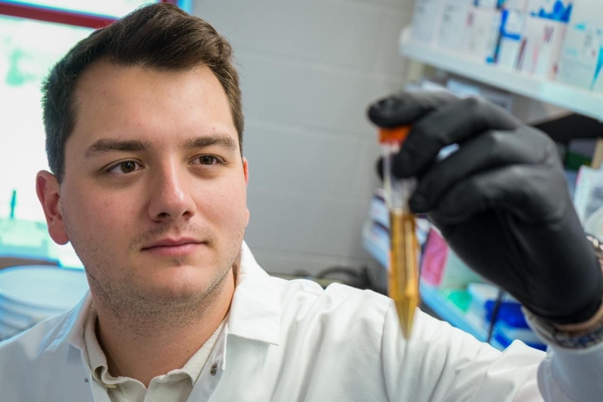 A dark haired man stands in a lab looking at a tube with yellow liquid at the Baker Institute. 