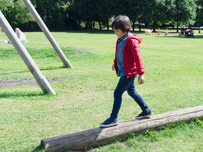 A child walking on a narrow tree trunk fallen in the grass