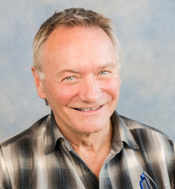 David Russel smiling while wearing a brown plaid button-up.