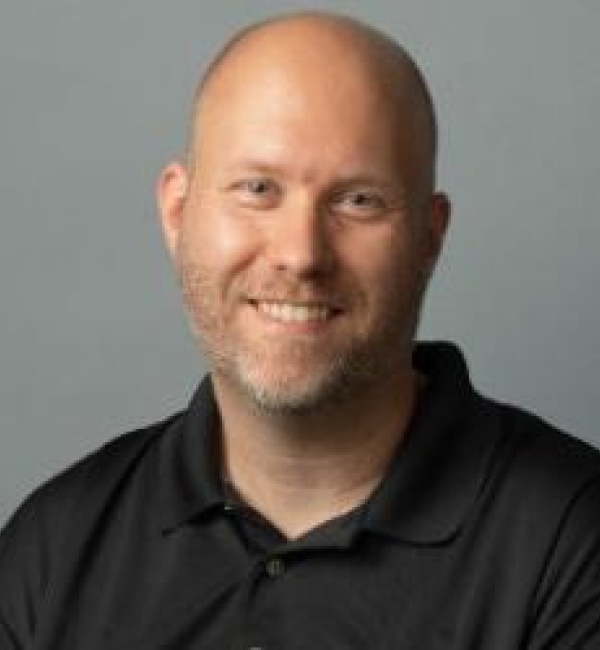 Nicolas Buchon wearing a black polo shirt in front of a gray background.