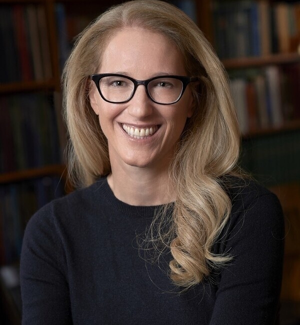 Raina Plowright sitting in front of a bookcase wearing a black long-sleeved shirt.
